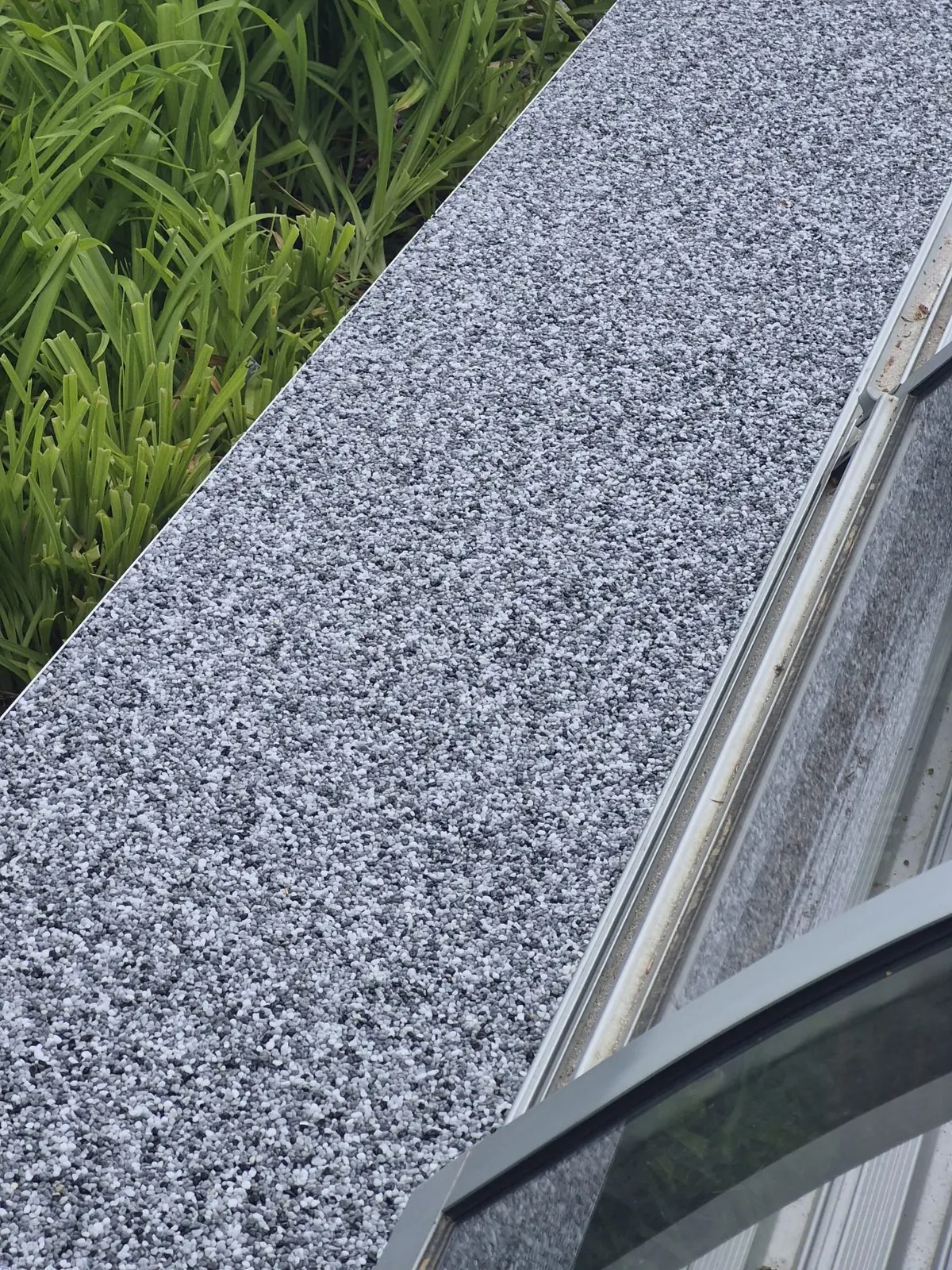 Detailaufnahme eines grauen Natursteinteppichs an einer Fensterfront